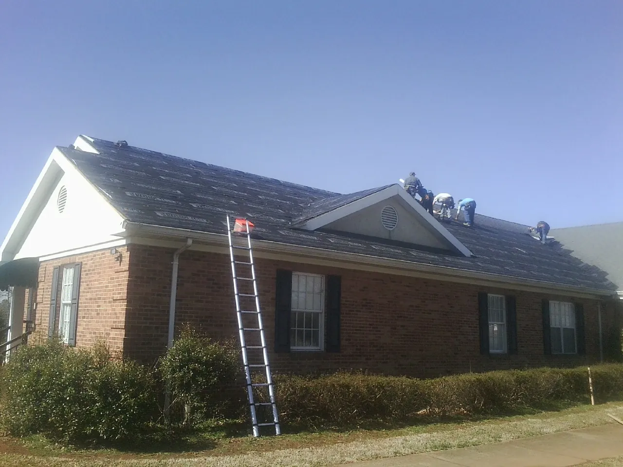 Crew tearing shingles off a brick ranch roof with a ladder set — Metal Roof Repair work by our crew in North Granby