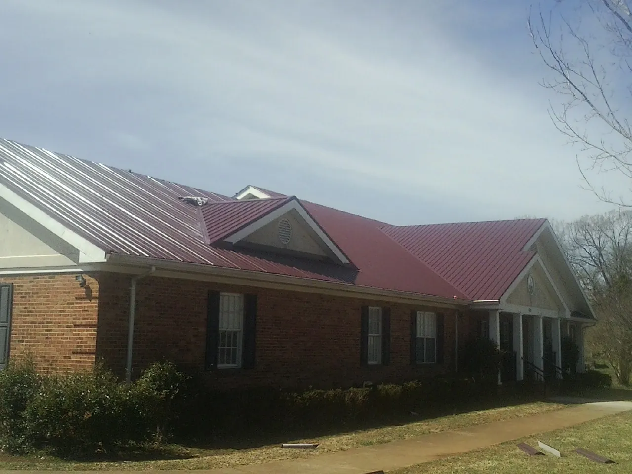 Red metal roof with gabled entries on a long brick building, from a Hail Damage Roof Repair job in North Granby