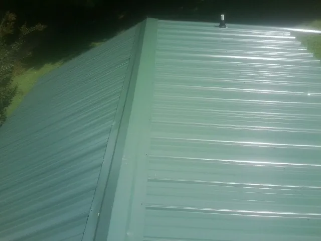 New green metal panels meeting at the ridge of a roof — Flat Roof Repair work by our crew in North Granby
