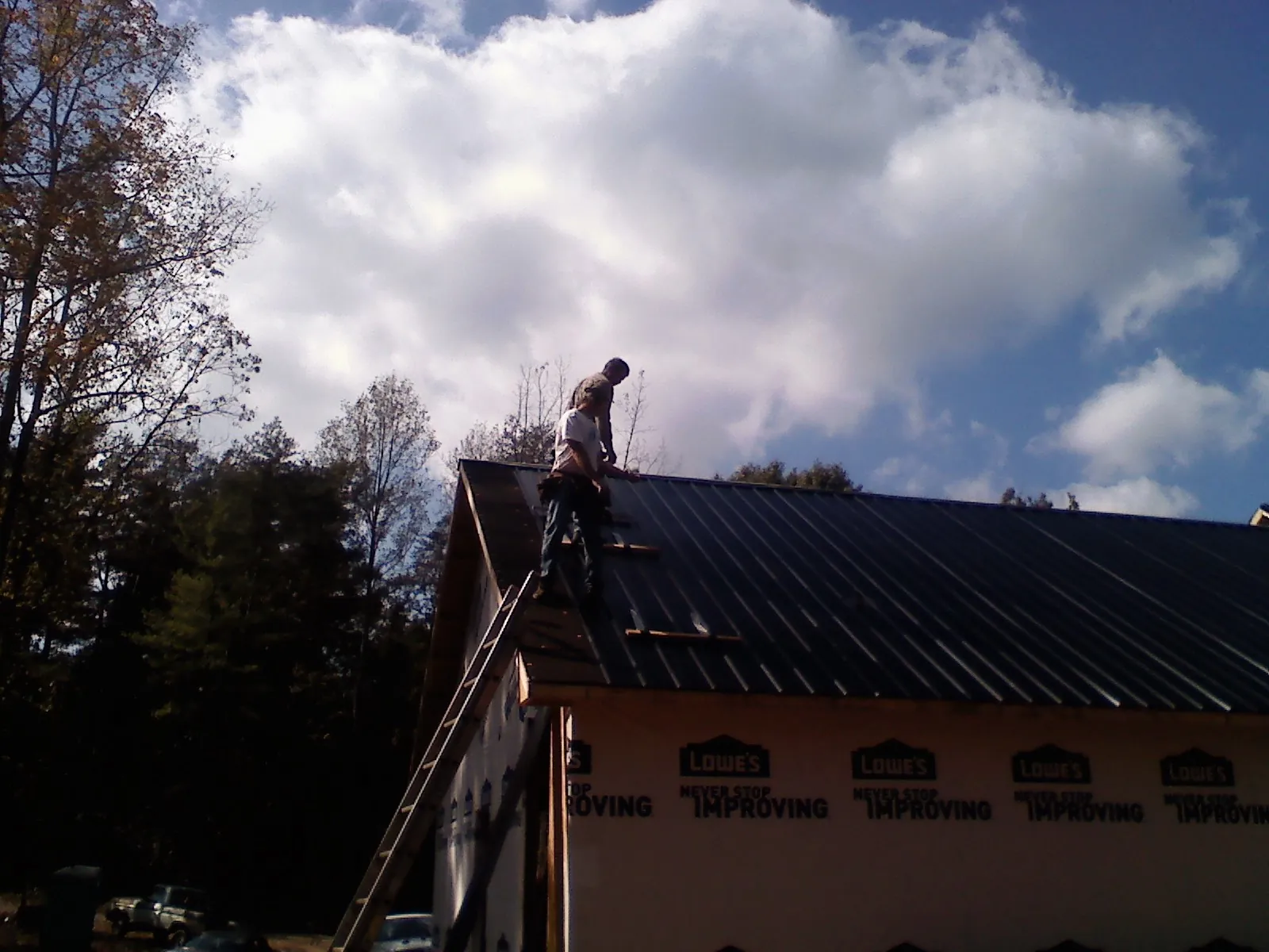 Roofer fastening dark metal panels high against a cloudy sky, from a Roof Inspection job in North Granby