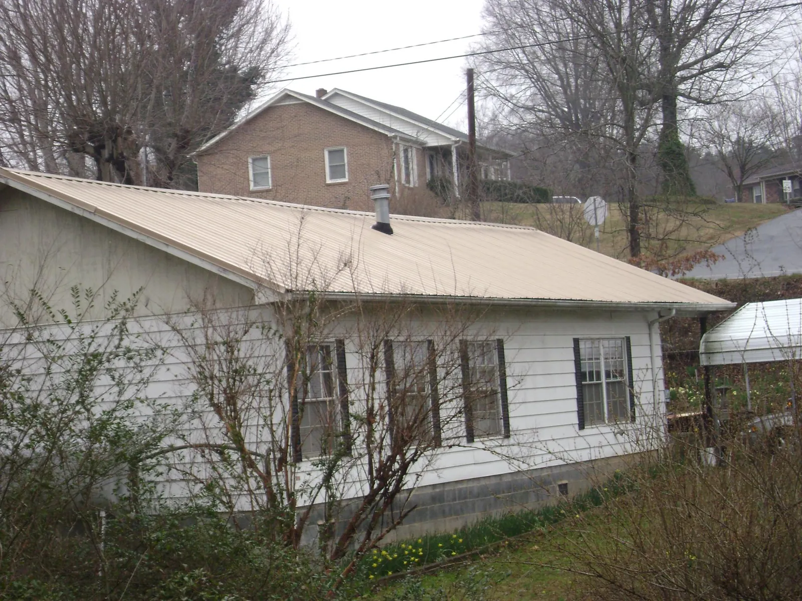 Tan metal roof on a white sided house set into a hillside — Commercial Roofing by Roofing Brothers in North Granby